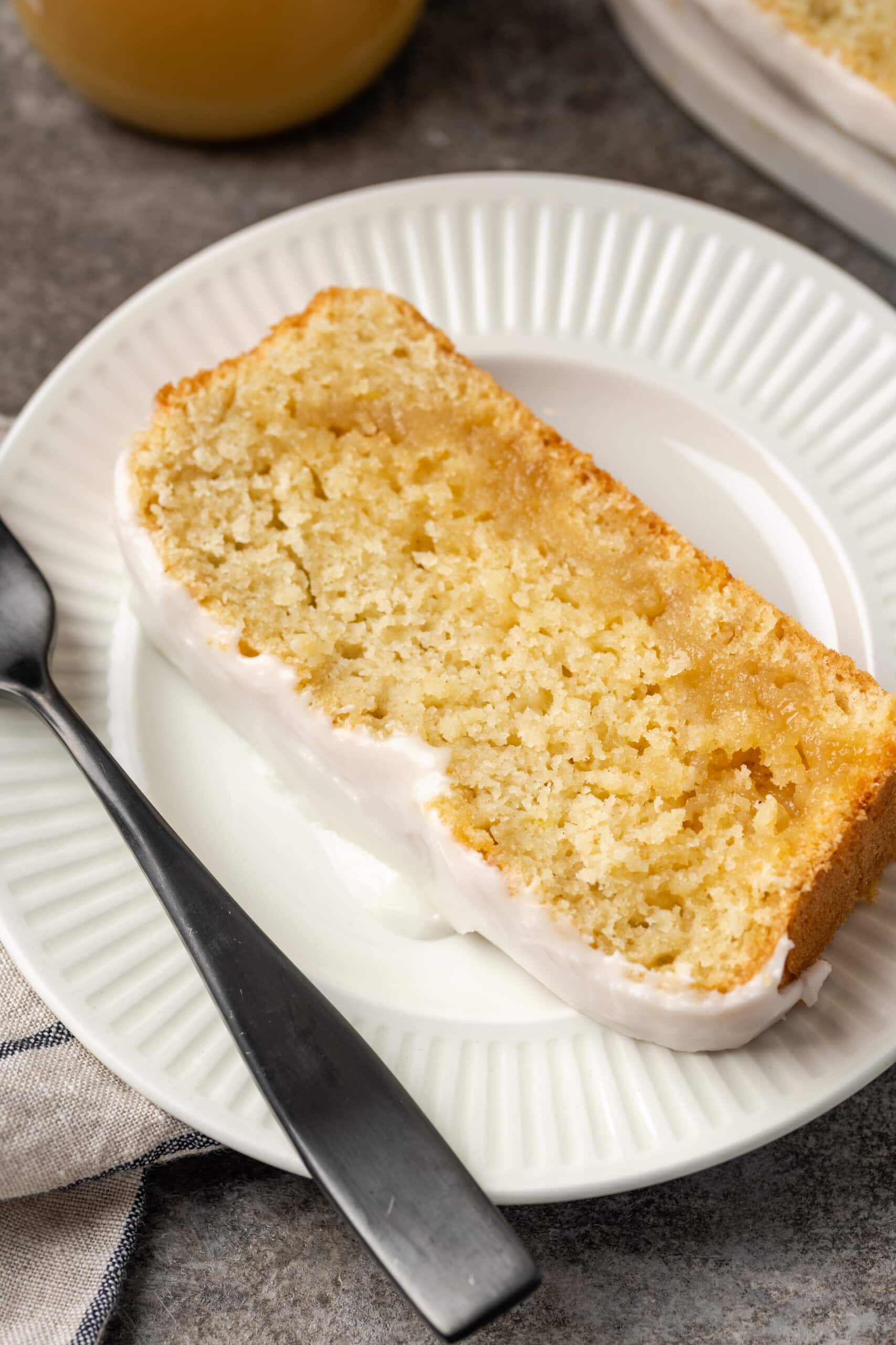 Una rebanada de bizcocho de limón glaseado en un plato blanco junto a un tenedor.