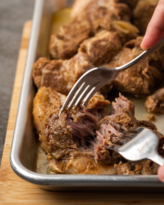 ¡Esta receta de Instant Pot Carnitas necesita solo 5 minutos de preparación! Haga carnitas increíblemente tiernas, jugosas y crujientes para tacos de cerdo y más. Dos tenedores utilizados para desmenuzar el asado de cerdo cocido en una bandeja para hornear de metal.