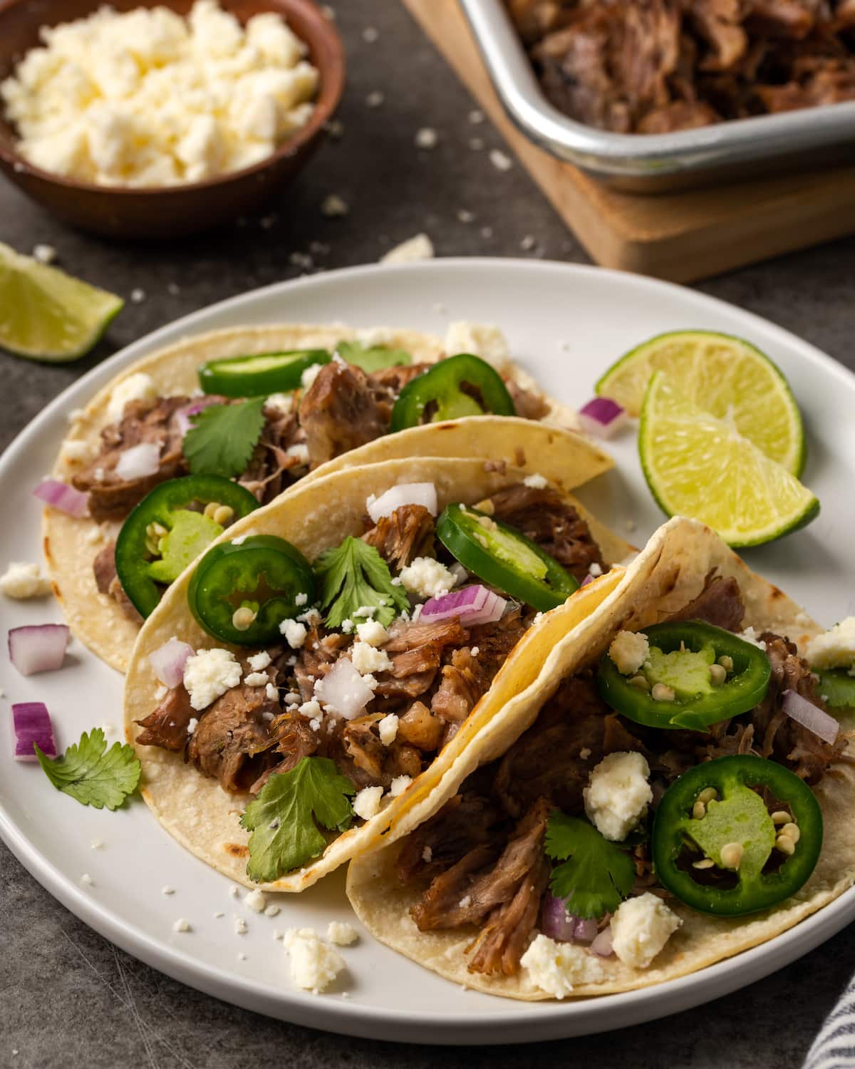 ¡Esta receta de Instant Pot Carnitas necesita solo 5 minutos de preparación! Haga carnitas increíblemente tiernas, jugosas y crujientes para tacos de cerdo y más. Tres tacos de cerdo cubiertos con jalapeños y queso en un plato blanco junto a rodajas de lima.