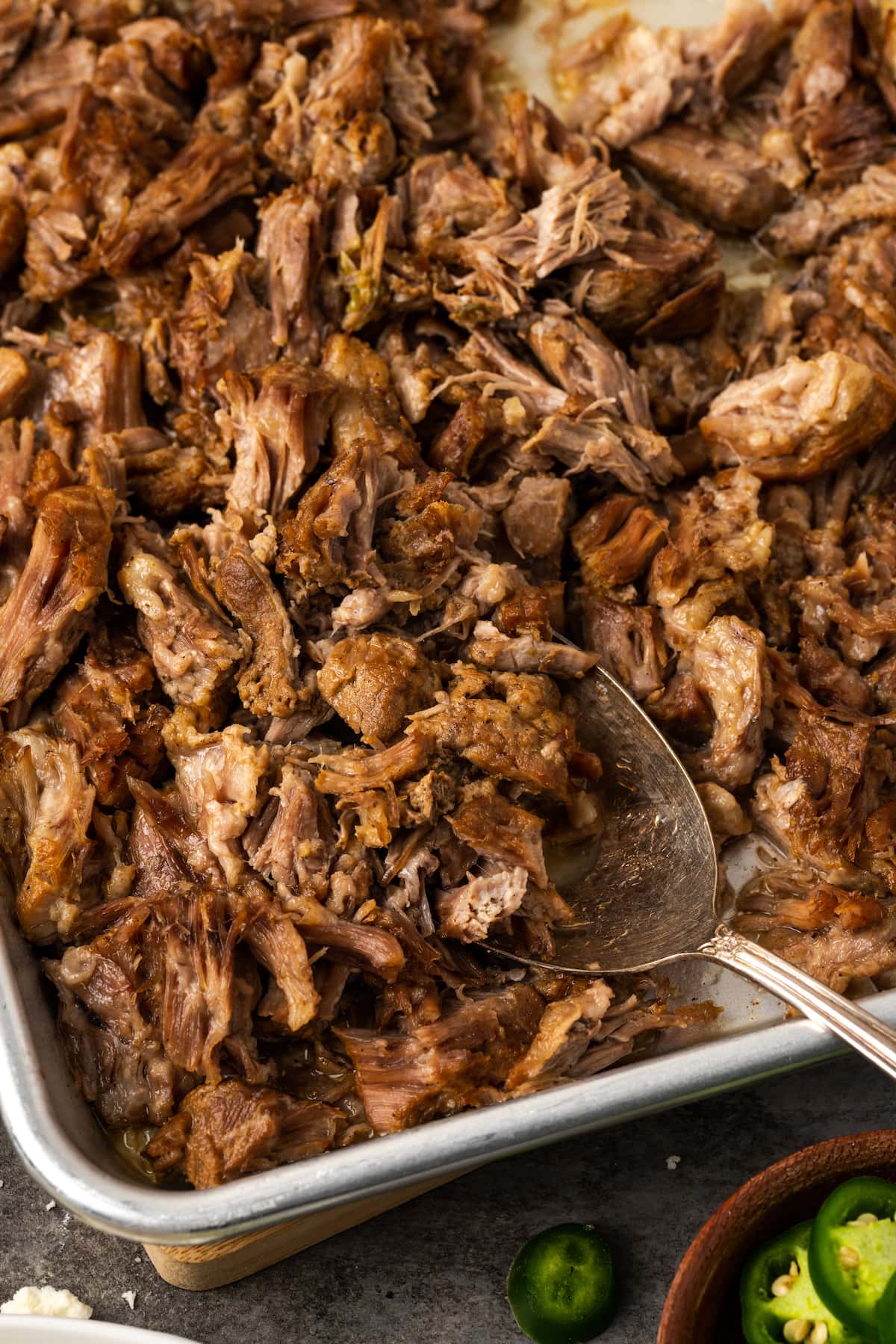 ¡Esta receta de Instant Pot Carnitas necesita solo 5 minutos de preparación! Haga carnitas increíblemente tiernas, jugosas y crujientes para tacos de cerdo y más. Vista aérea de carnitas instantáneas en una bandeja para hornear de metal con una cuchara.