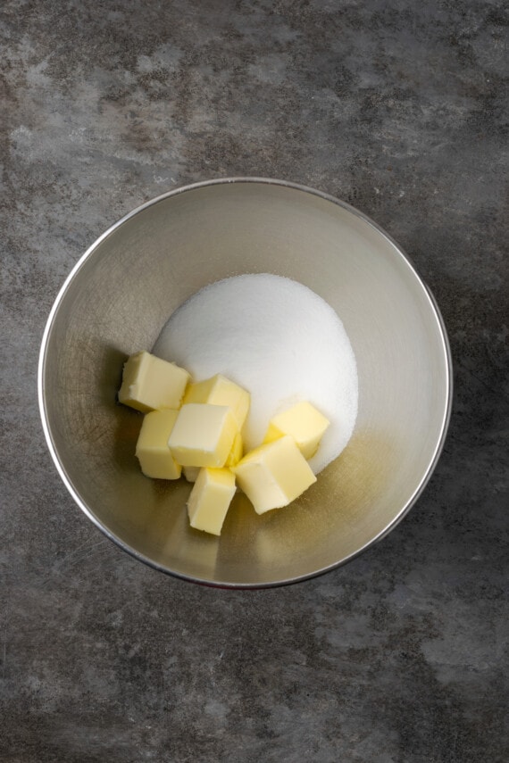 Esta receta de bizcocho Victoria es suave, esponjosa y está hecha con ingredientes simples. ¡Perfecto para combinar con mermelada y crema batida casera! Mantequilla en cubos y azúcar en un tazón de metal.