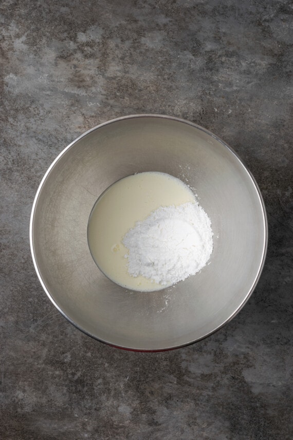 Esta receta de bizcocho Victoria es suave, esponjosa y está hecha con ingredientes simples. ¡Perfecto para combinar con mermelada y crema batida casera! Azúcar en polvo y crema espesa combinadas en un recipiente de metal.
