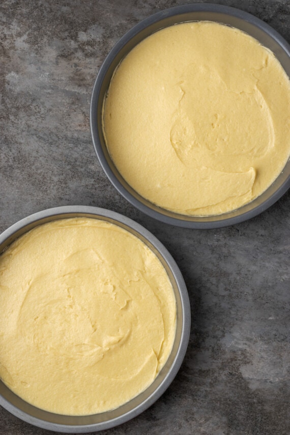 Esta receta de bizcocho Victoria es suave, esponjosa y está hecha con ingredientes simples. ¡Perfecto para combinar con mermelada y crema batida casera! Vista aérea de dos moldes para pasteles redondos llenos de masa de bizcocho.