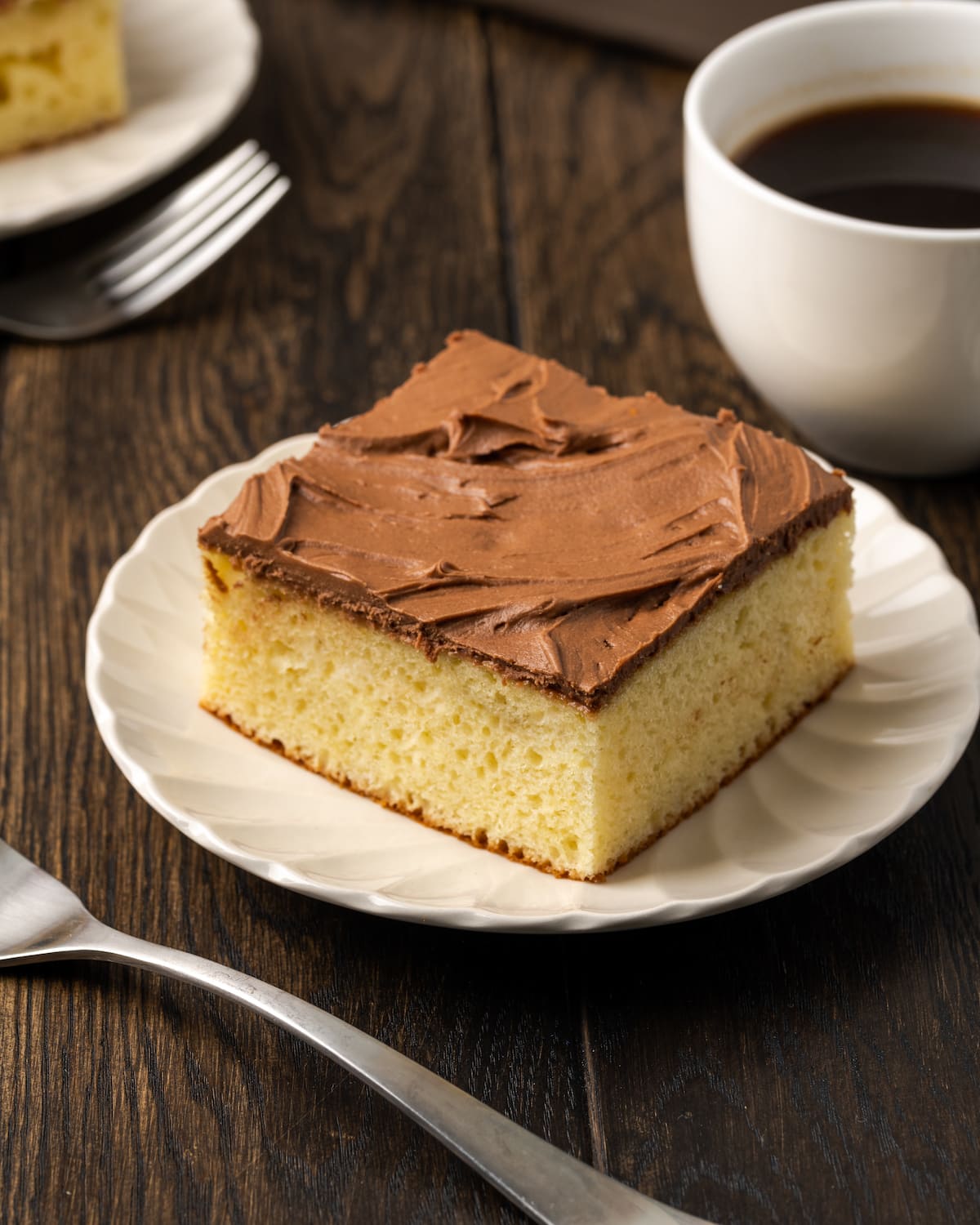 Una rebanada de pastel de crema agria helada en un plato blanco junto a un tenedor y una taza de café.