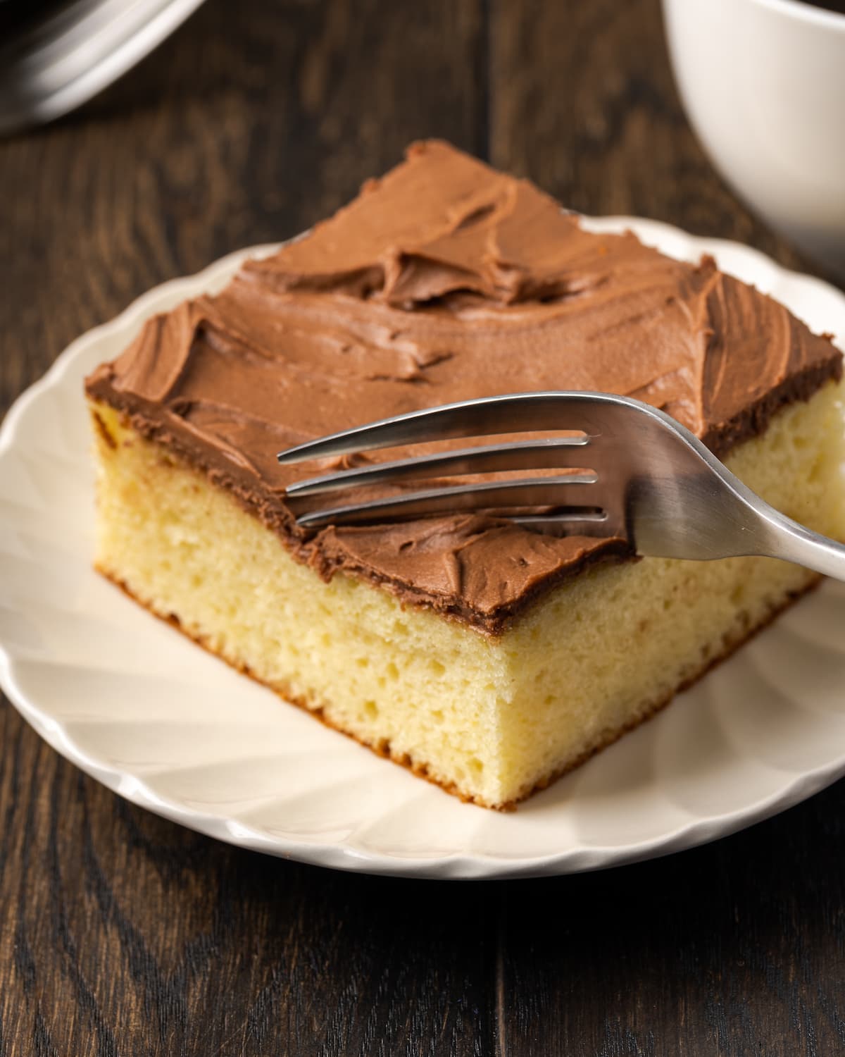 Un tenedor corta la esquina de una rebanada de pastel de crema agria helada en un plato blanco.