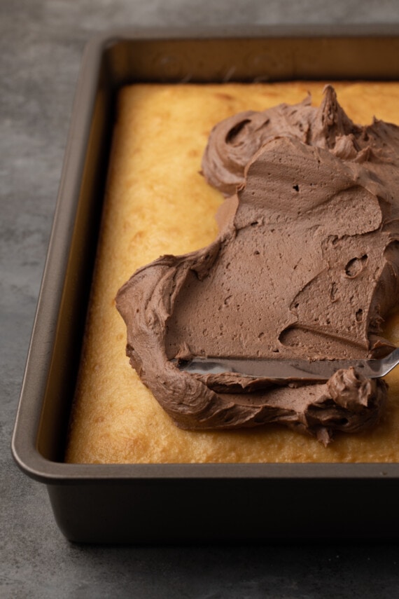 El glaseado de chocolate se extiende sobre un pastel de crema agria horneado en un molde para pasteles.