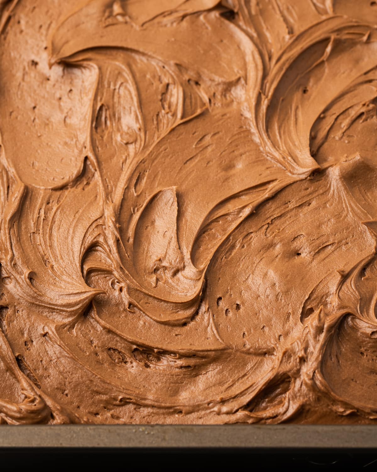 Cremoso glaseado de chocolate esparcido sobre un pastel de crema agria en un molde para hornear.