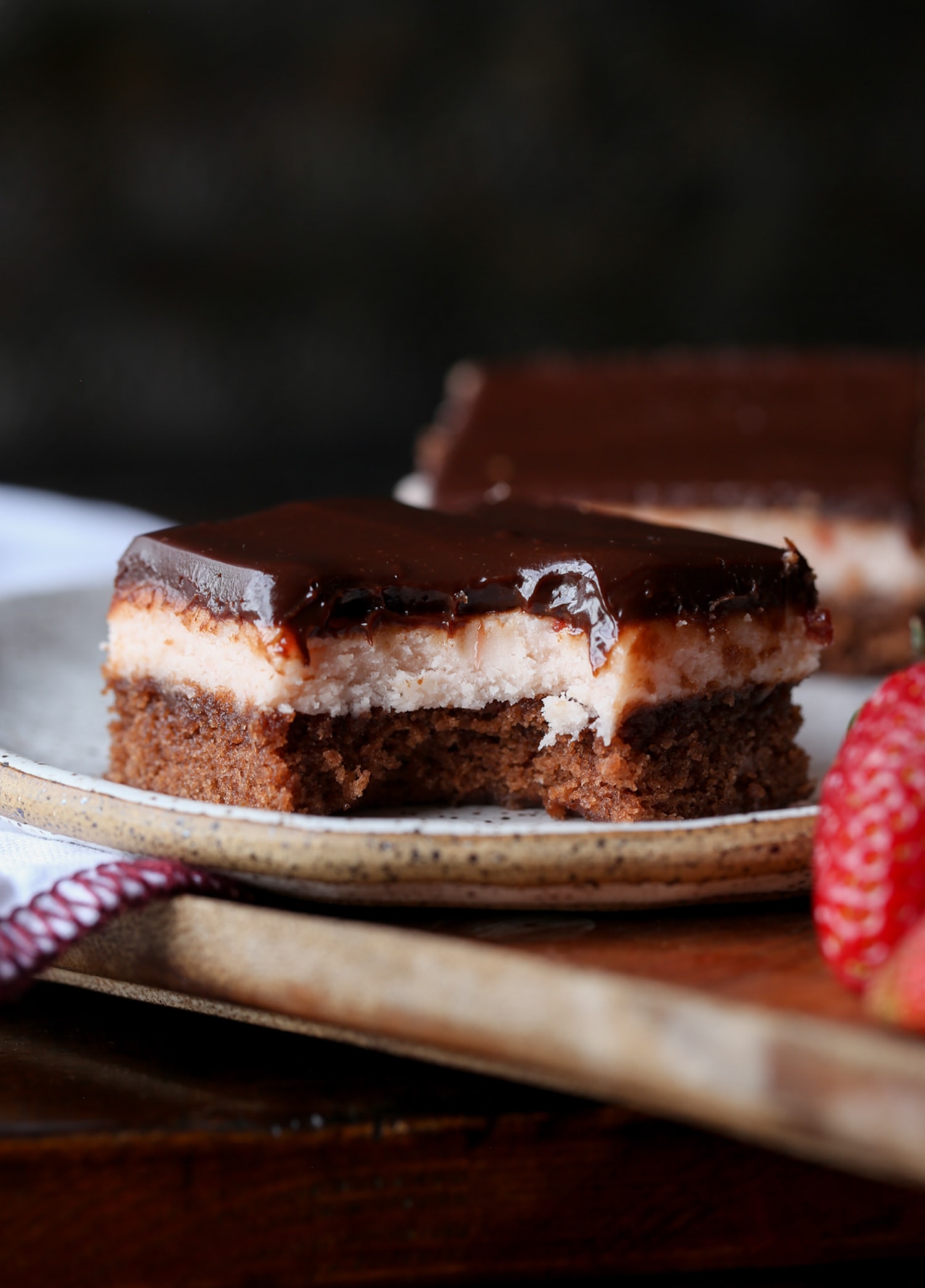 Un brownie de dulce de azúcar cubierto con crema de mantequilla de fresa y ganache de chocolate con un bocado sacado en un plato