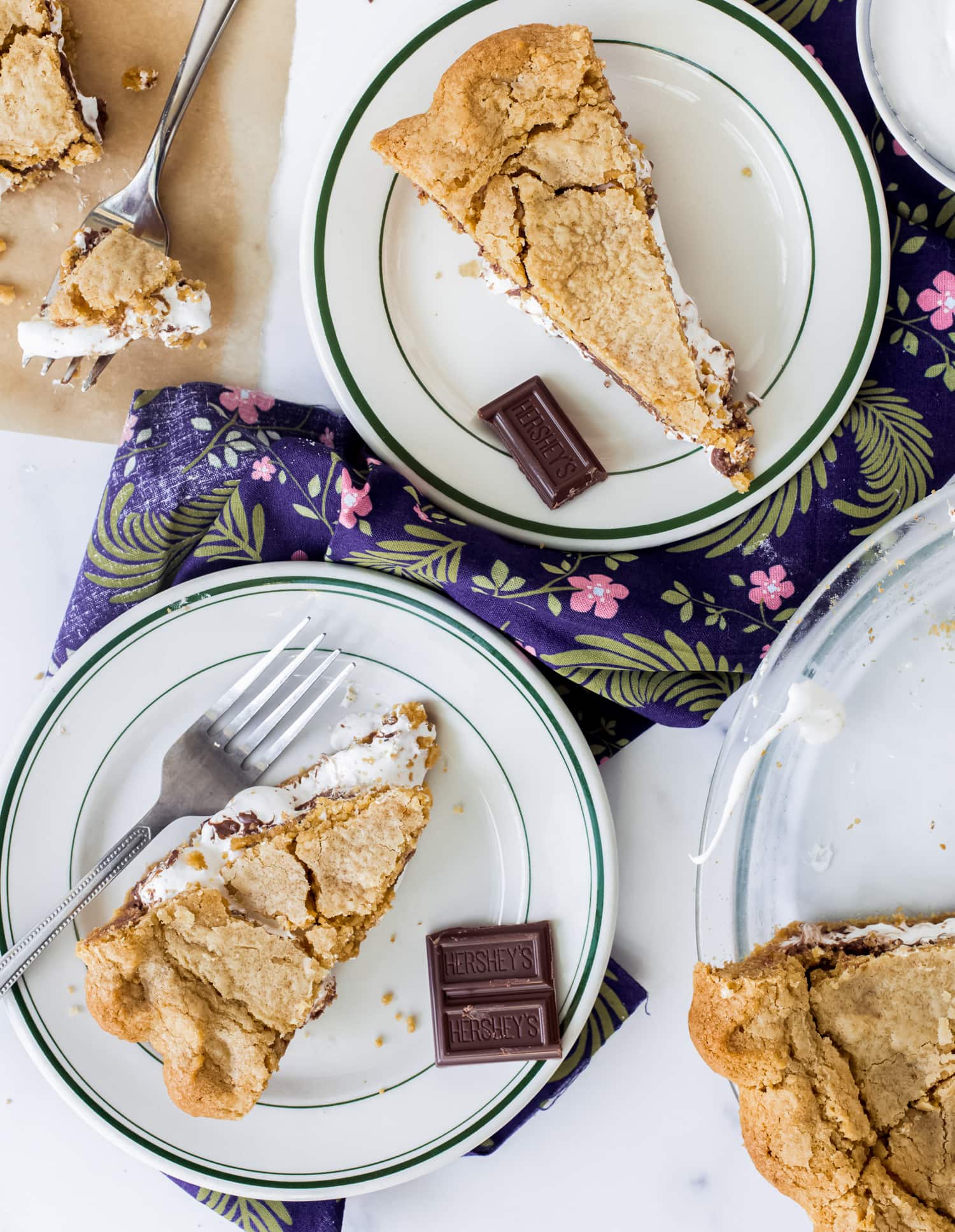 ¡Esta receta de Smores Pie es escandalosamente deliciosa! ¡La corteza de galleta Graham enrollada es única y fácil, y el pastel está lleno de malvavisco pegajoso y chocolate derretido! ¡Como una rebanada gigante de smores sin necesidad de fogata! rebanadas de pastel de s'mores en platos tomados desde arriba
