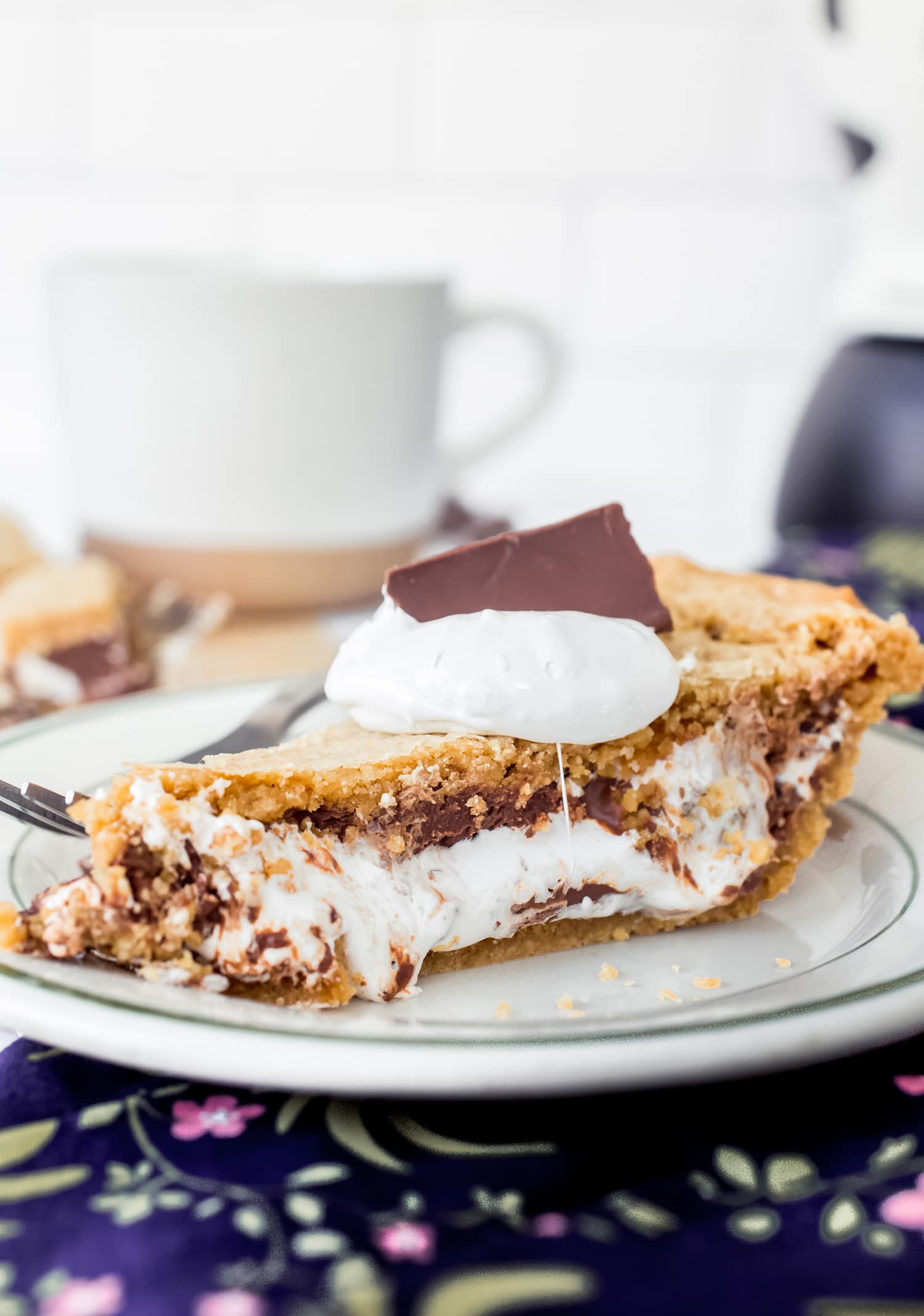 ¡Esta receta de Smores Pie es escandalosamente deliciosa! ¡La corteza de galleta Graham enrollada es única y fácil, y el pastel está lleno de malvavisco pegajoso y chocolate derretido! ¡Como una rebanada gigante de smores sin necesidad de fogata! Una rebanada de pastel de s'mores en un plato cubierto con crema de malvavisco y un trozo de chocolate