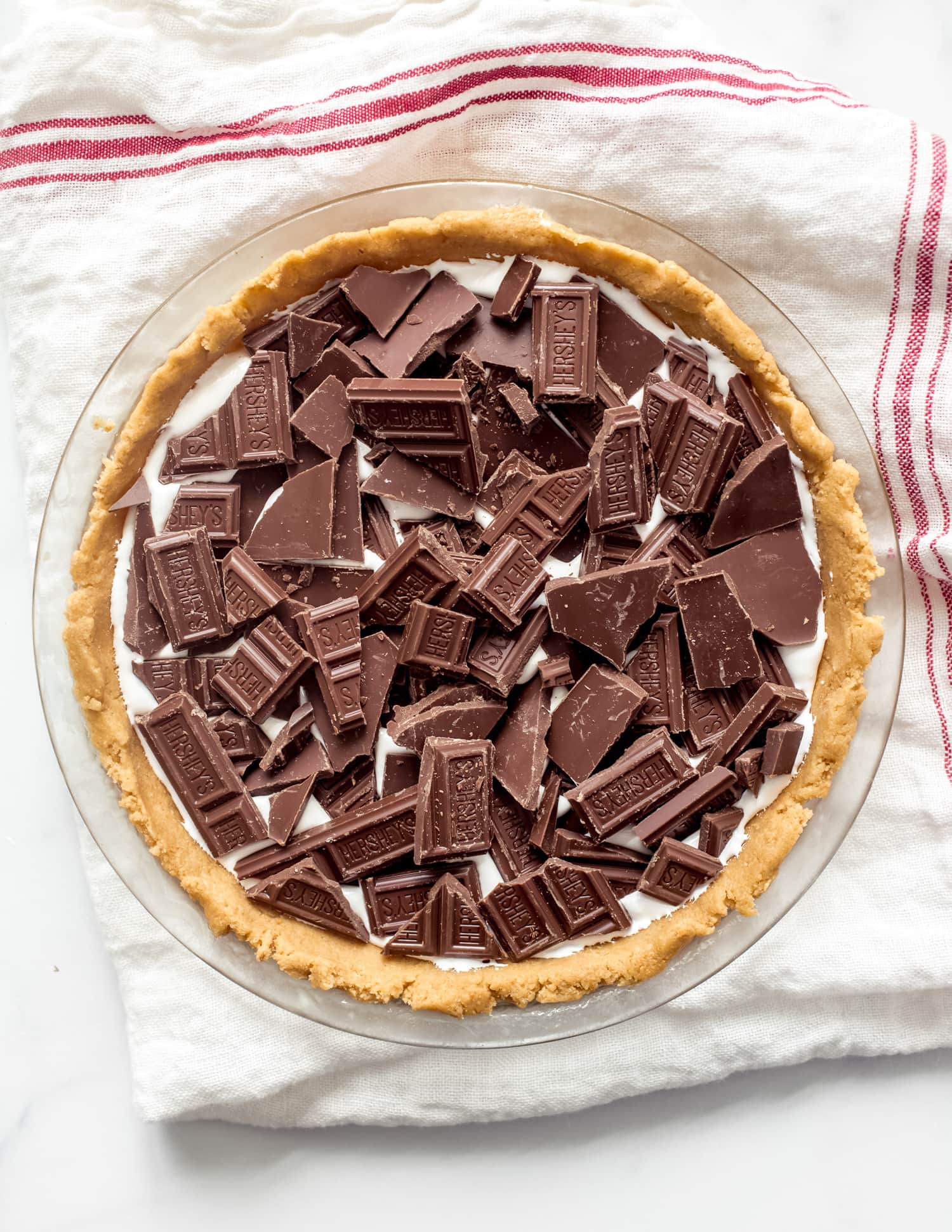 ¡Esta receta de Smores Pie es escandalosamente deliciosa! ¡La corteza de galleta Graham enrollada es única y fácil, y el pastel está lleno de malvavisco pegajoso y chocolate derretido! ¡Como una rebanada gigante de smores sin necesidad de fogata! Un pastel de arriba relleno con pelusa de malvavisco y chocolate Hershey antes de hornearse.