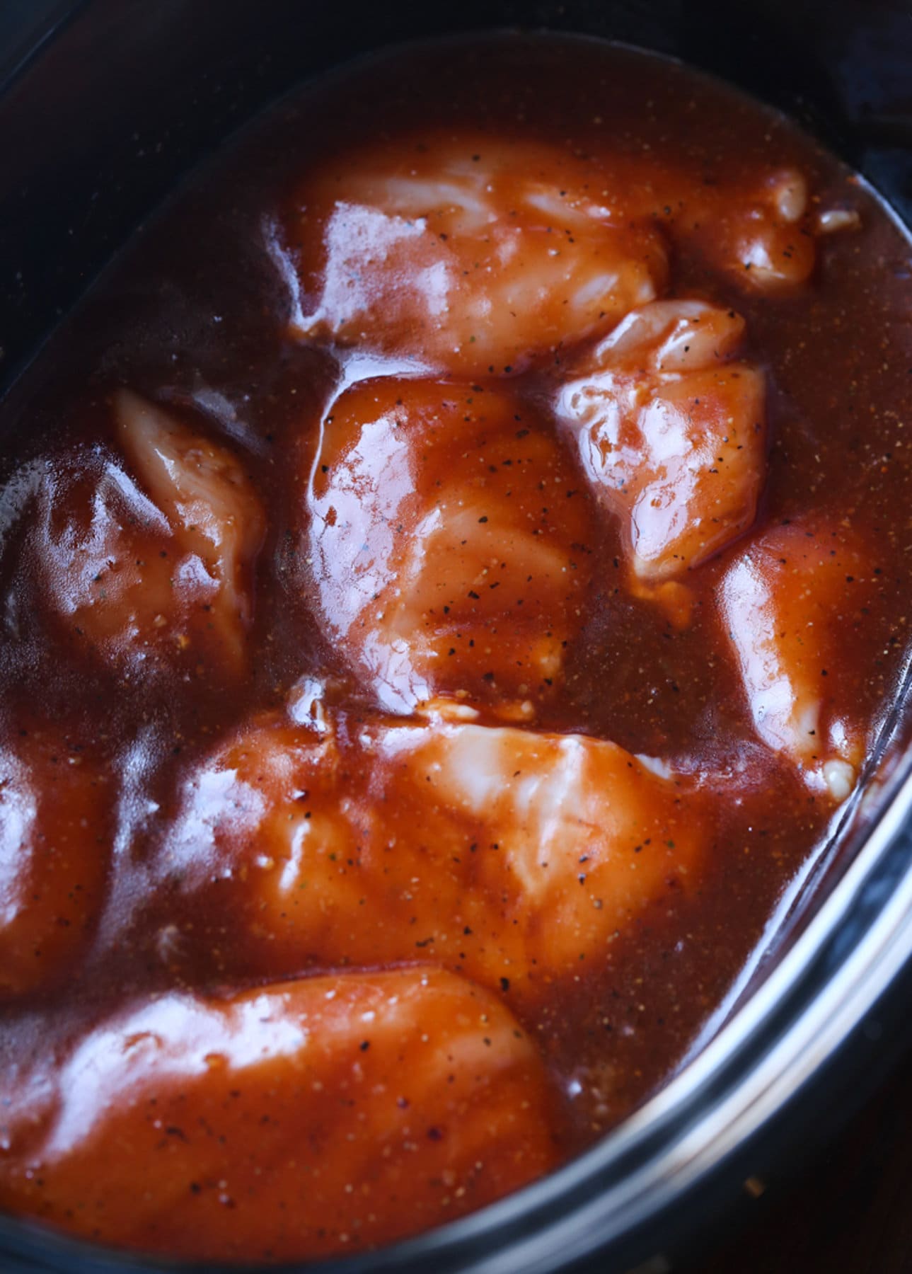 pollo crudo en una olla de cocción lenta crockpot cubierto con salsa BBQ