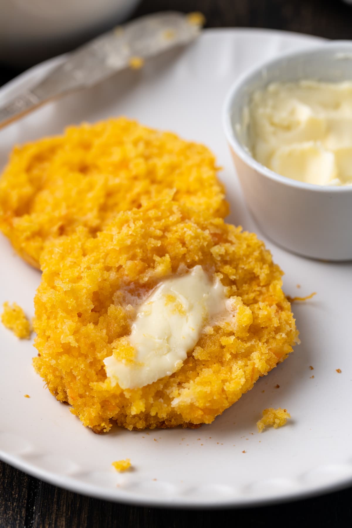 Primer plano de una galleta de camote cortada por la mitad y untada con mantequilla en un plato, al lado de un pequeño plato de mantequilla.