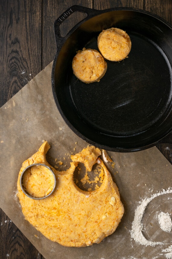Se utiliza un cortador de galletas redondo para cortar la masa de galletas de boniato junto a dos galletas en una sartén de hierro fundido.