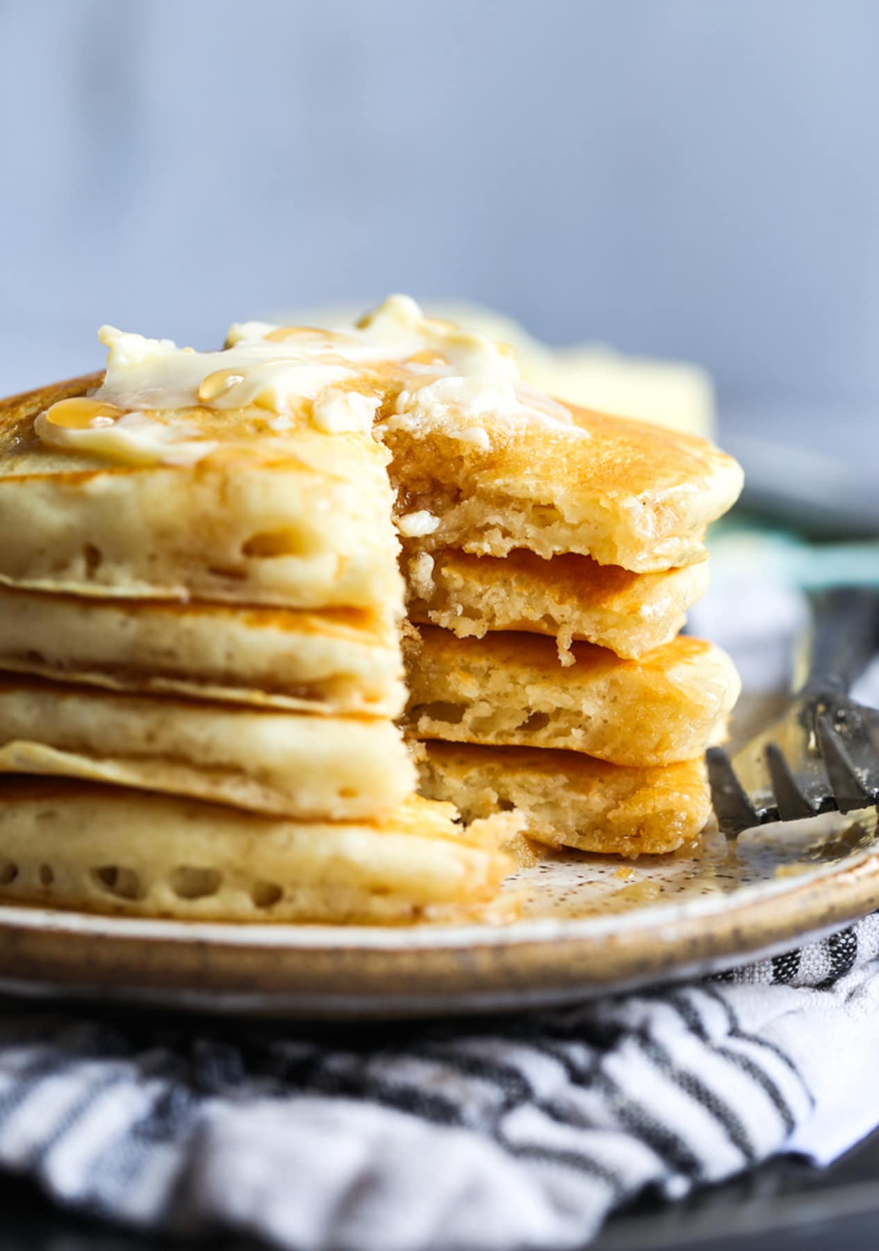 Panqueques de suero de leche apilados en un plato con mantequilla y jarabe cortados para mostrar el interior esponjoso