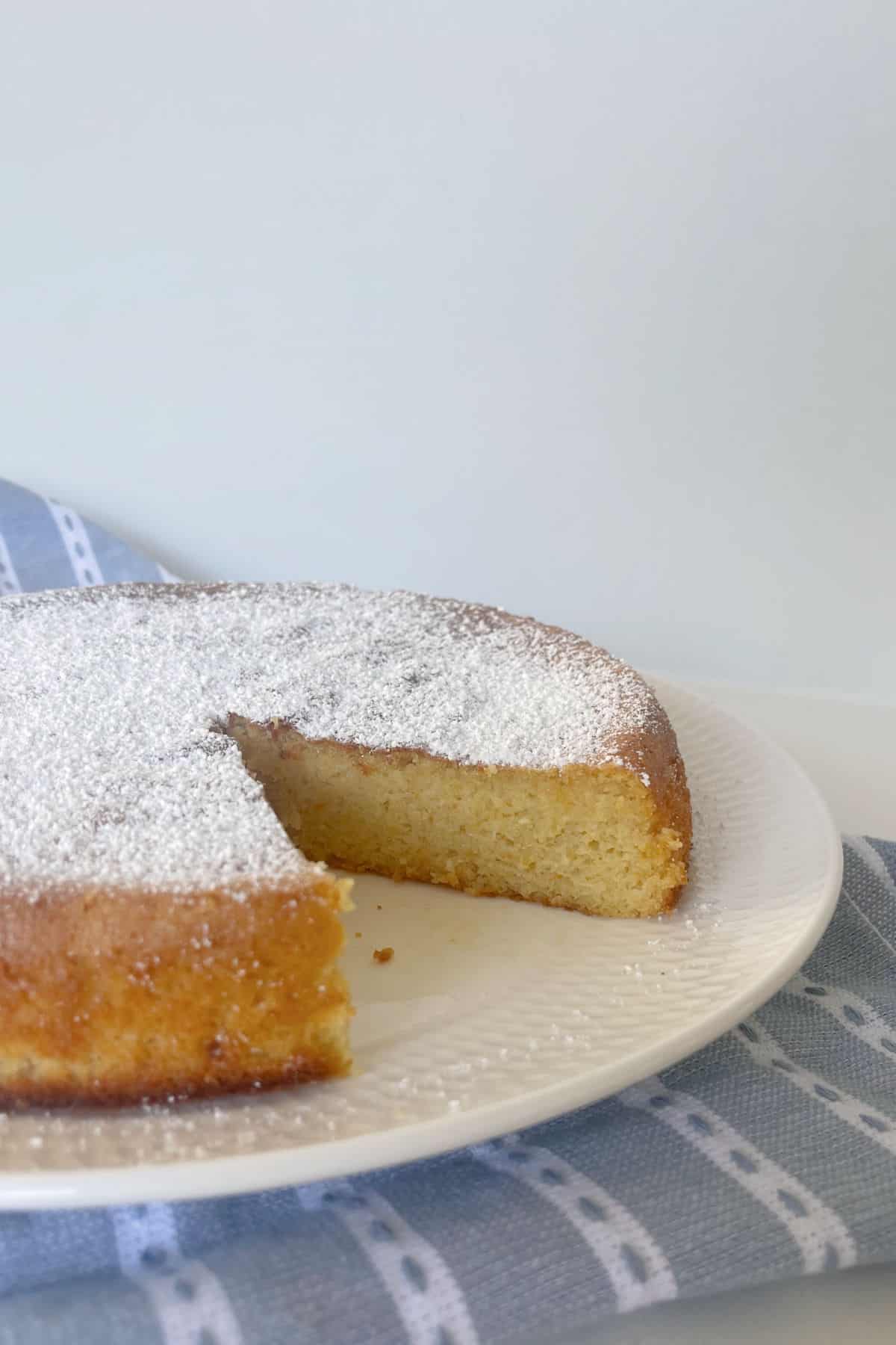 Pastel de naranja entero espolvoreado con azúcar glas sobre un plato blanco.