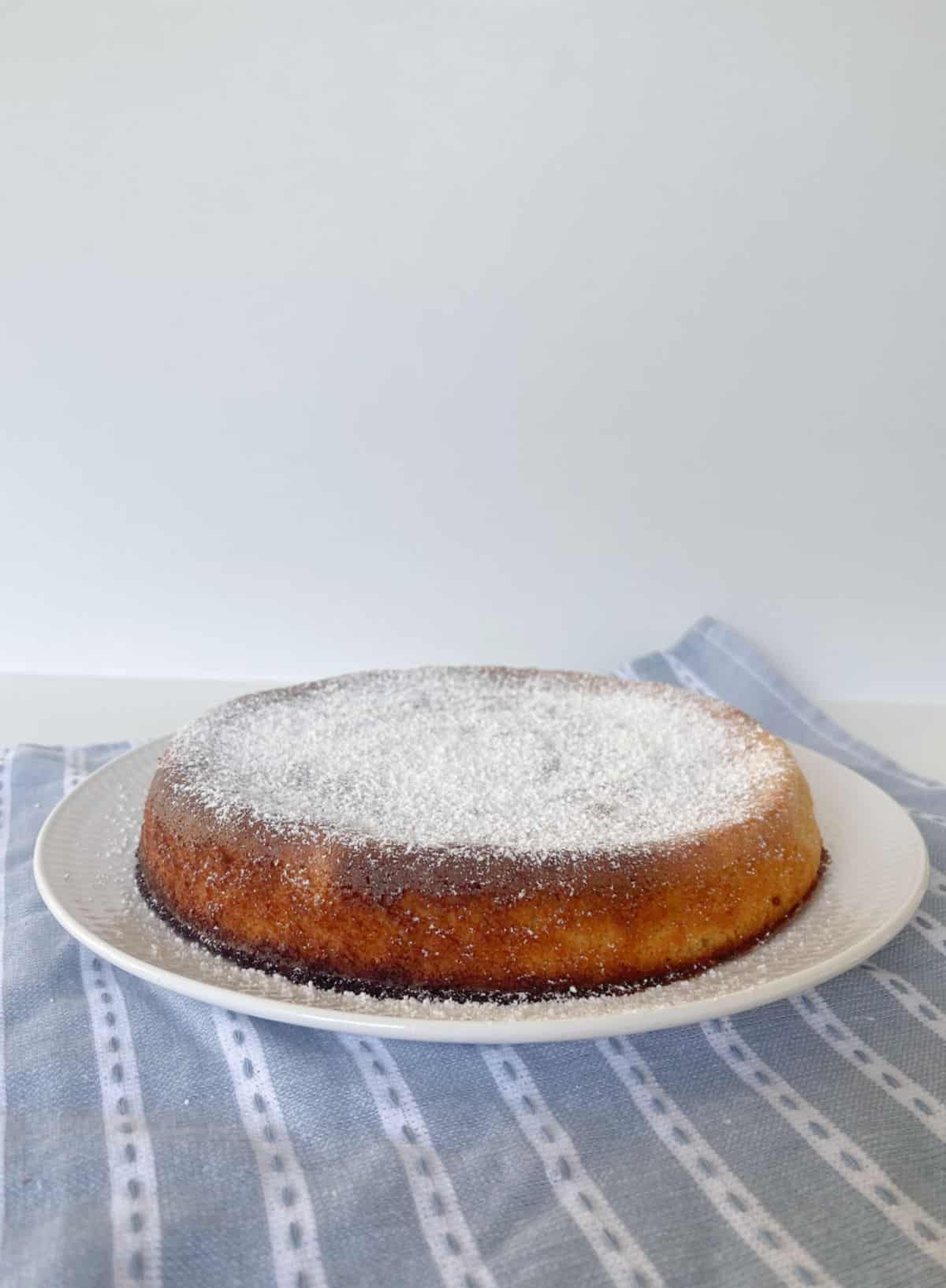 Vista lateral de Whole Orange Cake espolvoreado con azúcar glaseado sentado en un plato blanco.