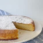 Pastel de naranja entero espolvoreado con azúcar glas sobre un plato blanco.