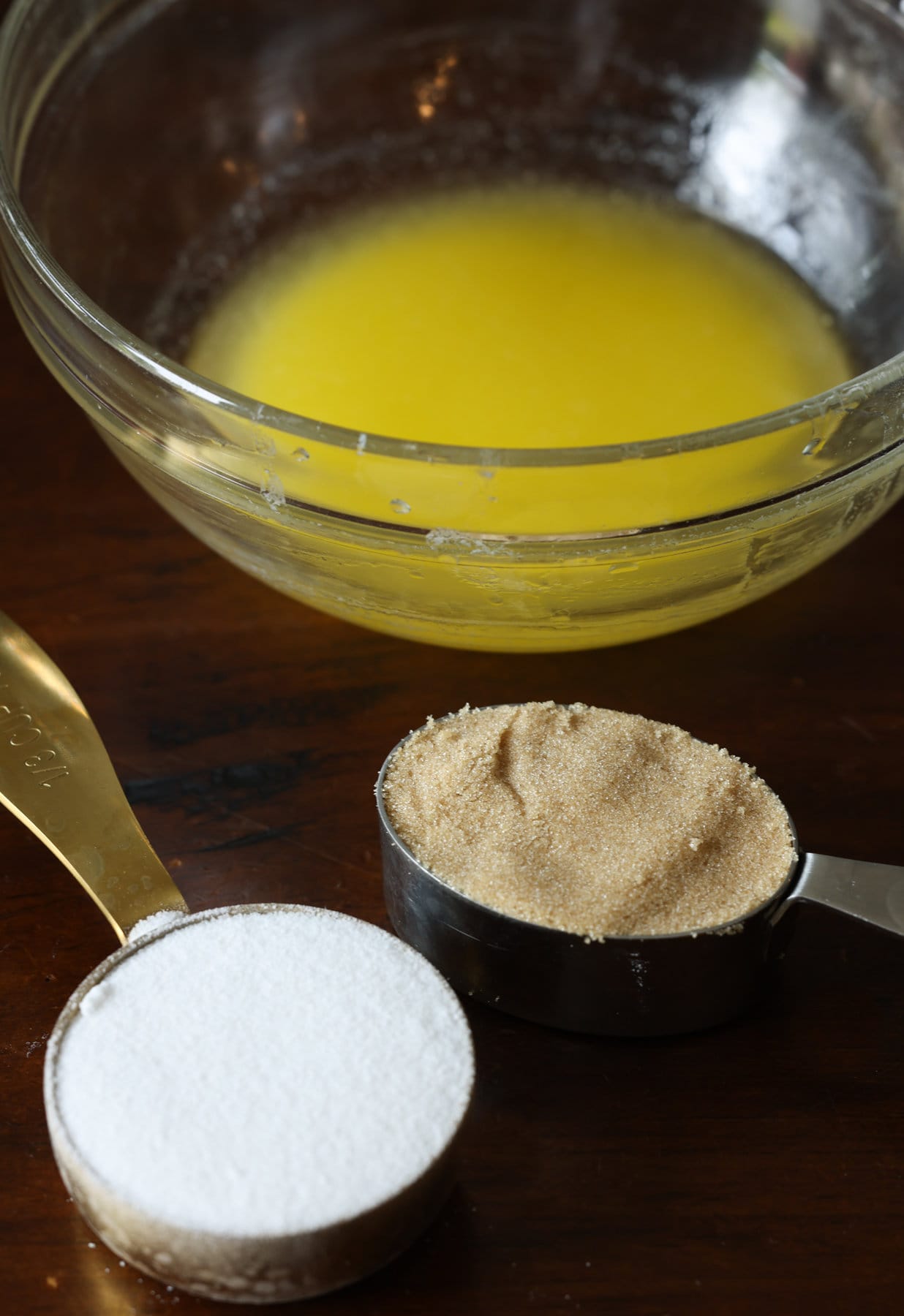 Streusel Topping, también conocido como Crumb Topping, es muy fácil de hacer y se puede usar en muchos productos horneados diferentes, desde muffins y panes hasta pasteles y tartas, ¡o se hornea solo y se usa como una cobertura crujiente de mantequilla! Ingredientes para la cobertura de streusel sobre una mesa, la mantequilla derretida en un recipiente de vidrio, azúcar granulada y azúcar moreno claro en tazas medidoras