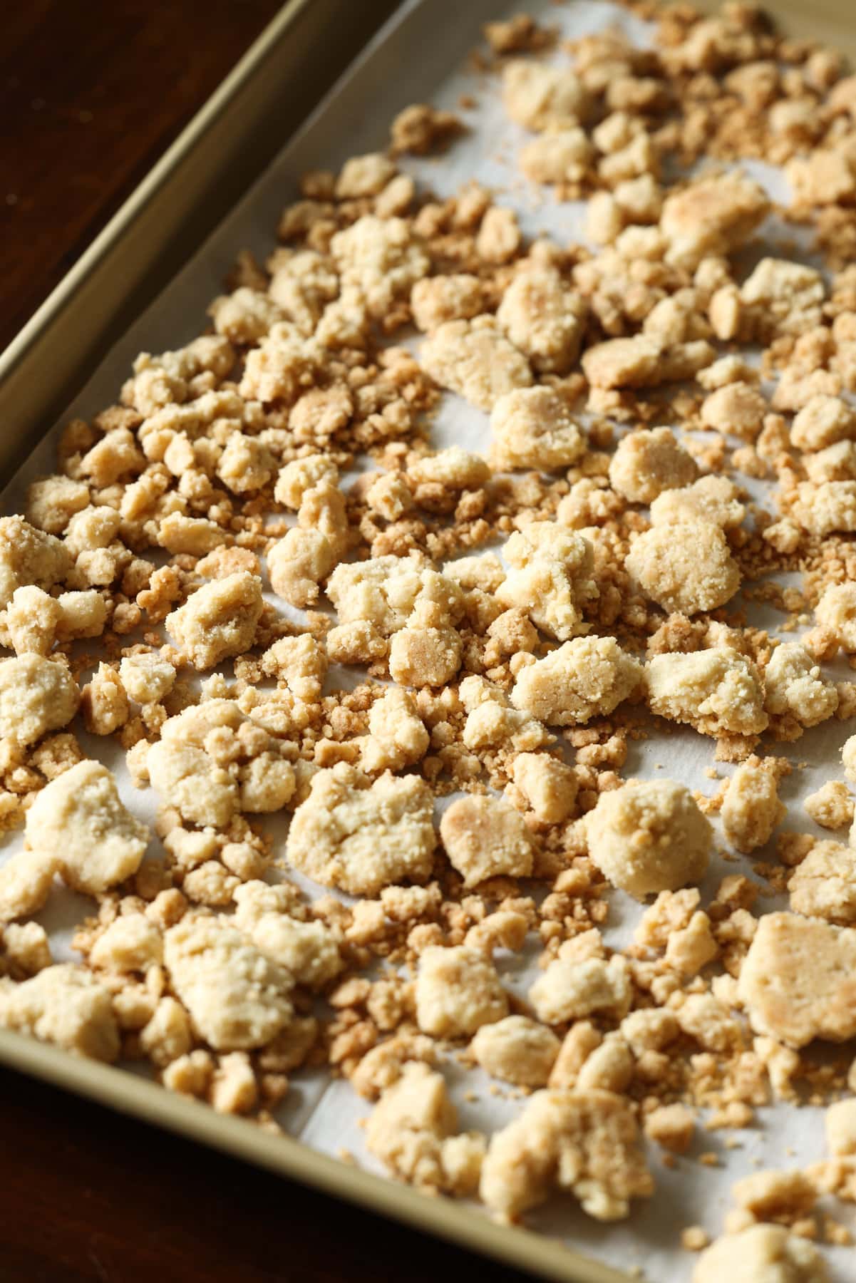 Streusel Topping, también conocido como Crumb Topping, es fácil de hacer y se puede usar en muchos productos horneados diferentes, desde muffins y panes hasta pasteles y tartas. Streusel Topping horneado en una bandeja para hornear forrada de pergamino