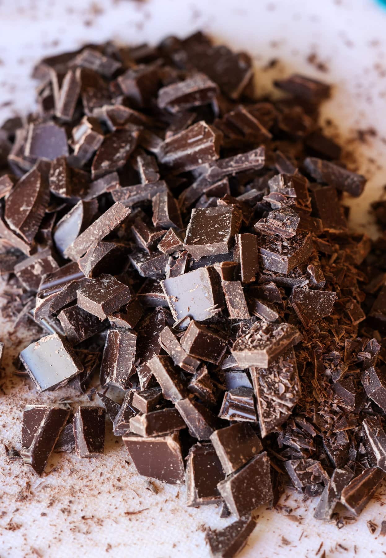 Mi Receta Blondie es la perfección. Barras de galletas masticables y mantecosas tachonadas con chispas de chocolate y mezcladas con coco dulce. Trozos de chocolate cortados en una tabla de cortar blanca