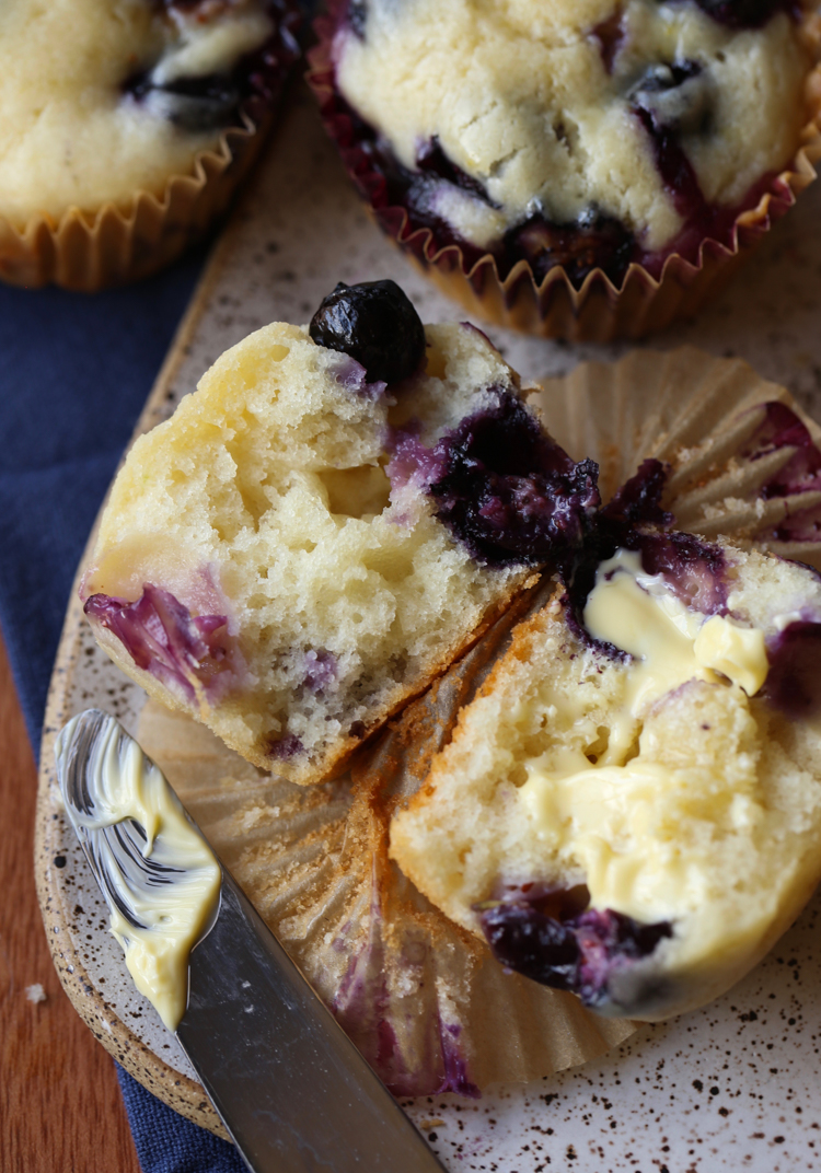 Dos mitades de un esponjoso muffin de arándanos con mantequilla en un plato.