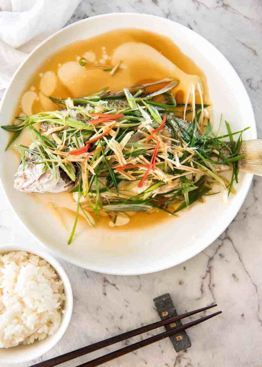 Un pescado al vapor chino cubierto con jengibre y chalotes y condimentos, con aceite caliente vertido sobre él para crear un chisporroteo dramático y una salsa increíble.  Tan simple, pero tan absolutamente delicioso.  ¡Cocine al vapor O hornee el pescado!  recetatineats.com