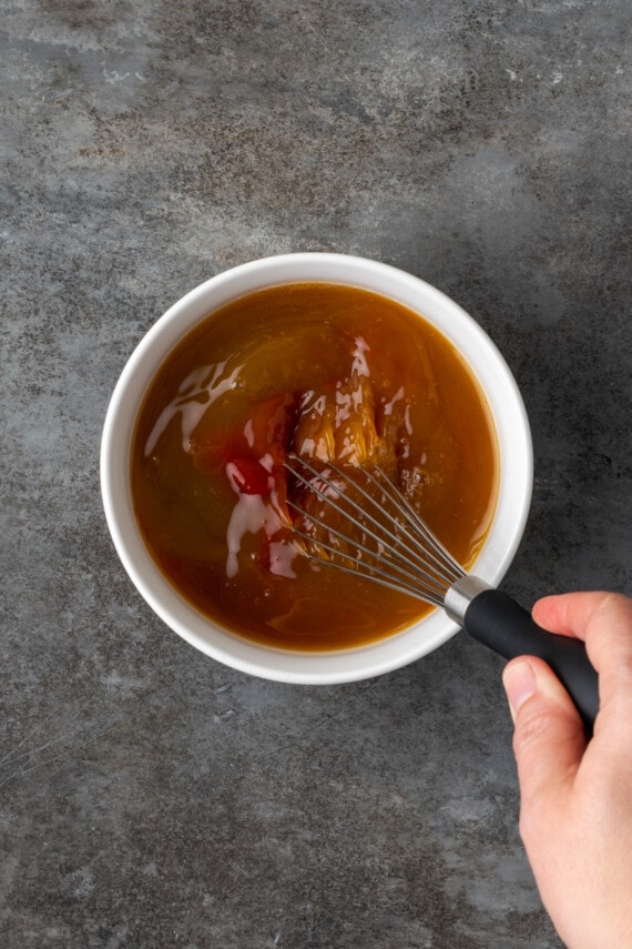 Instant Pot Hawaiian Chicken es una cena fácil de una olla cocinada con piña jugosa, pimientos y cebollas en una salsa dulce y picante. El jugo de piña se bate en la salsa para el pollo hawaiano en un tazón blanco.