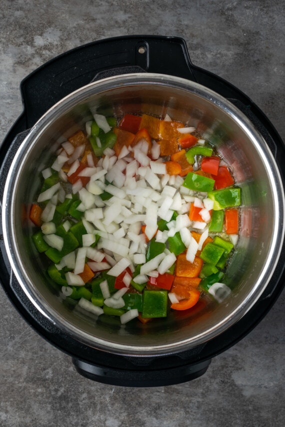 Instant Pot Hawaiian Chicken es una cena fácil de una olla cocinada con piña jugosa, pimientos y cebollas en una salsa dulce y picante. Cebollas picadas agregadas a Instant Pot con trozos de pimiento rojo y verde salteados.