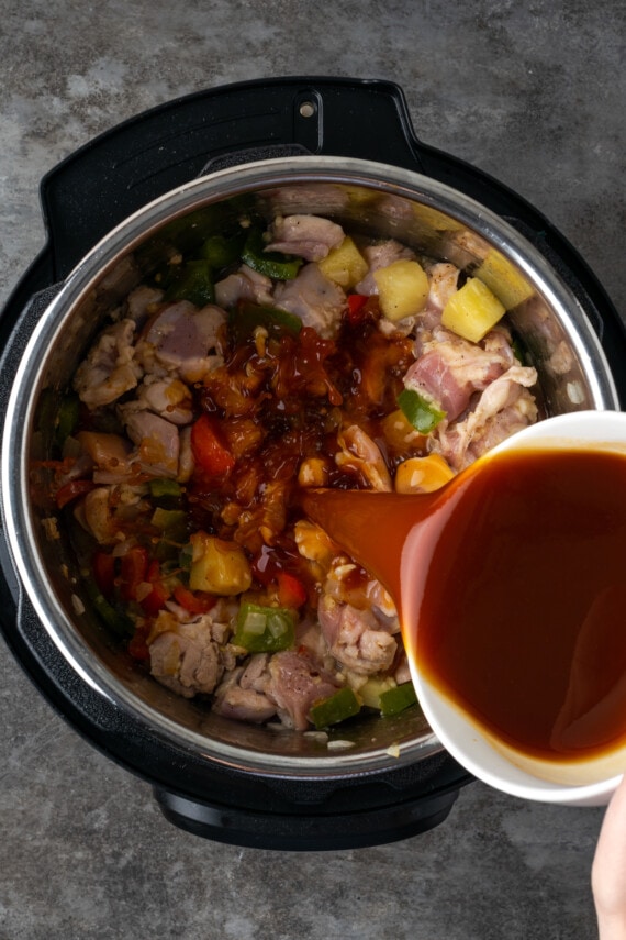 Instant Pot Hawaiian Chicken es una cena fácil de una olla cocinada con piña jugosa, pimientos y cebollas en una salsa dulce y picante. La salsa se vierte sobre los ingredientes de pollo hawaiano dentro de Instant Pot.