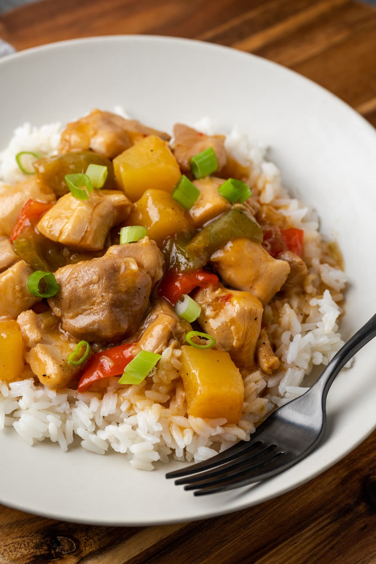 Instant Pot Hawaiian Chicken es una cena fácil de una olla cocinada con piña jugosa, pimientos y cebollas en una salsa dulce y picante. Instant Pot Hawaiian pollo servido sobre arroz en un plato blanco junto a un tenedor.