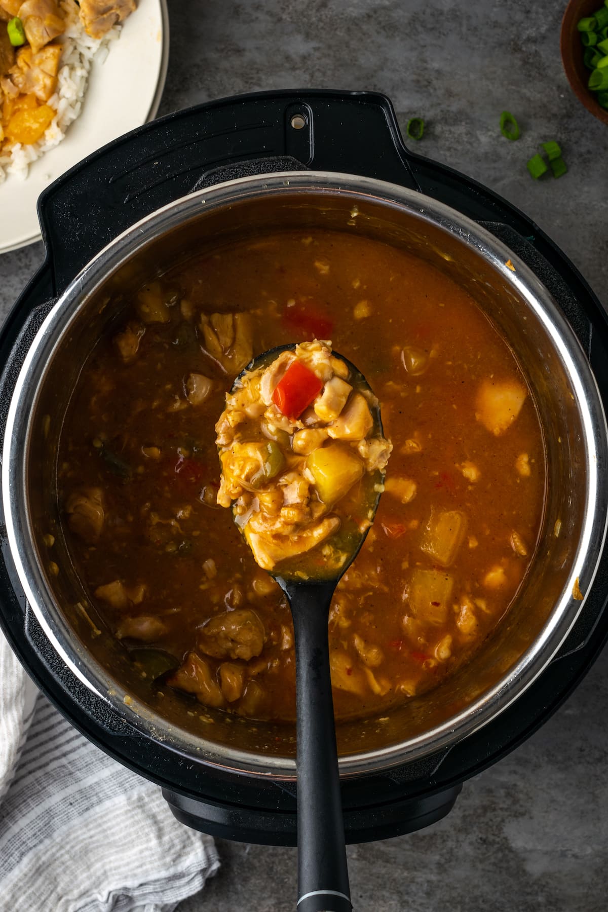 Instant Pot Hawaiian Chicken es una cena fácil de una olla cocinada con piña jugosa, pimientos y cebollas en una salsa dulce y picante. Vista aérea de una cucharada de pollo hawaiano sostenida sobre la Instant Pot.
