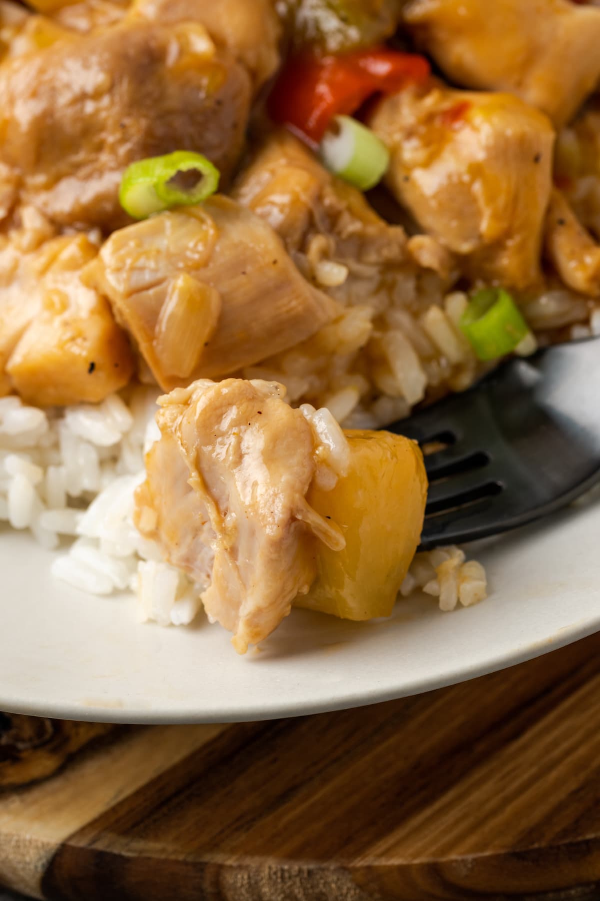 Instant Pot Hawaiian Chicken es una cena fácil de una olla cocinada con piña jugosa, pimientos y cebollas en una salsa dulce y picante. Un bocado de pollo hawaiano en un plato blanco junto a más pollo servido con arroz.
