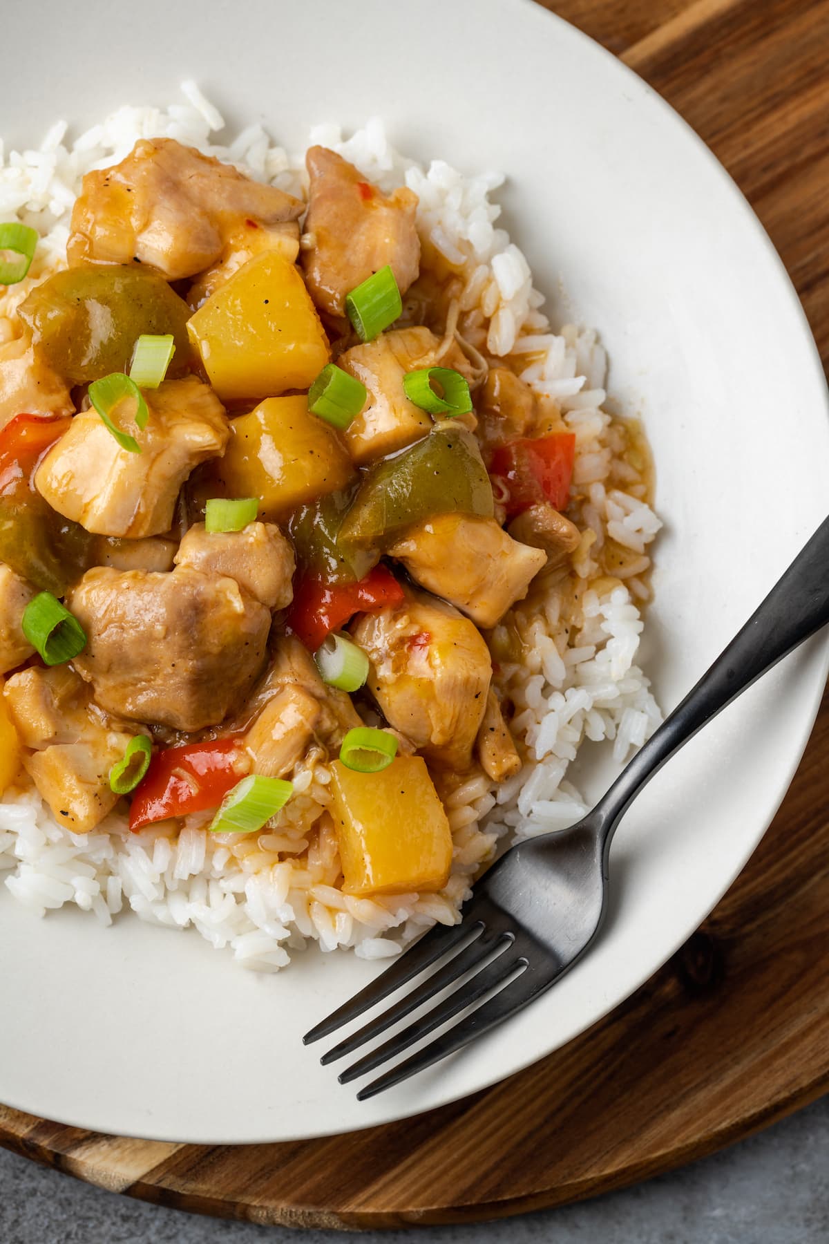 Instant Pot Hawaiian Chicken es una cena fácil de una olla cocinada con piña jugosa, pimientos y cebollas en una salsa dulce y picante. Vista aérea del pollo Instant Pot Hawaiian servido sobre arroz en un plato blanco junto a un tenedor.