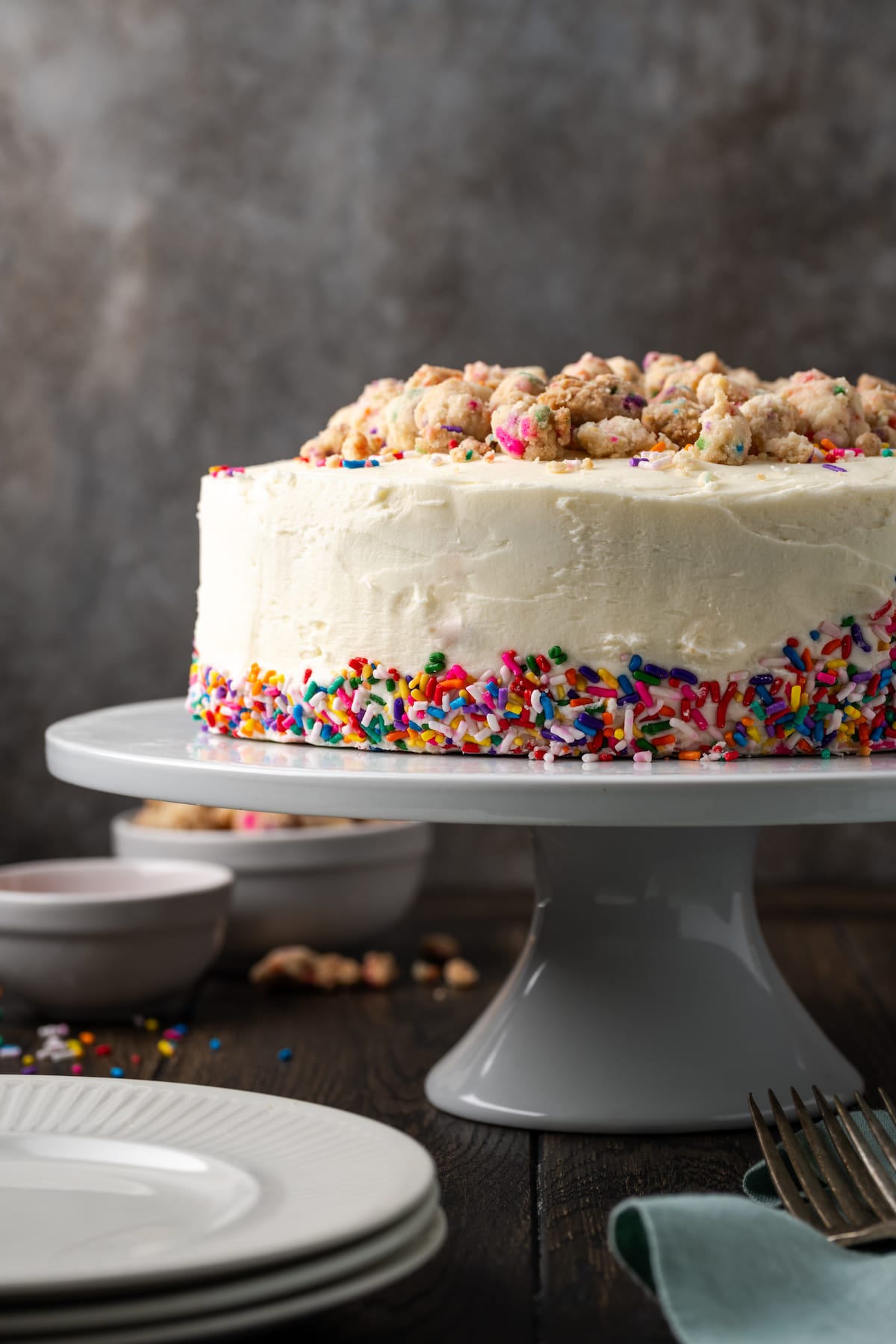 This is the best confetti cake recipe made from fluffy white cake loaded with rainbow sprinkles. Even better than a boxed Funfetti cake mix! Frosted confetti cake decorated with sprinkles on a white cake stand.