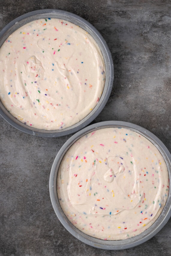 This is the best confetti cake recipe made from fluffy white cake loaded with rainbow sprinkles. Even better than a boxed Funfetti cake mix! Overhead view of two round cake pans filled with confetti cake batter.