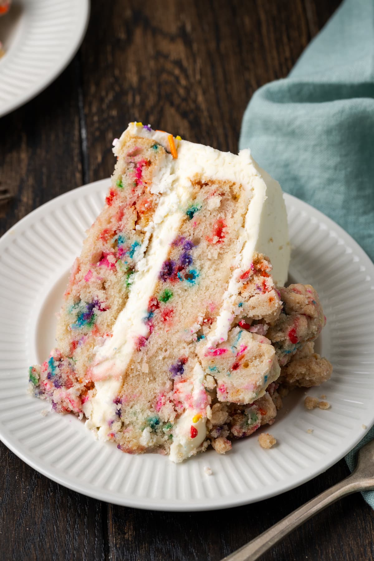 This is the best confetti cake recipe made from fluffy white cake loaded with rainbow sprinkles. Even better than a boxed Funfetti cake mix! A slice of frosted confetti cake on a white plate.
