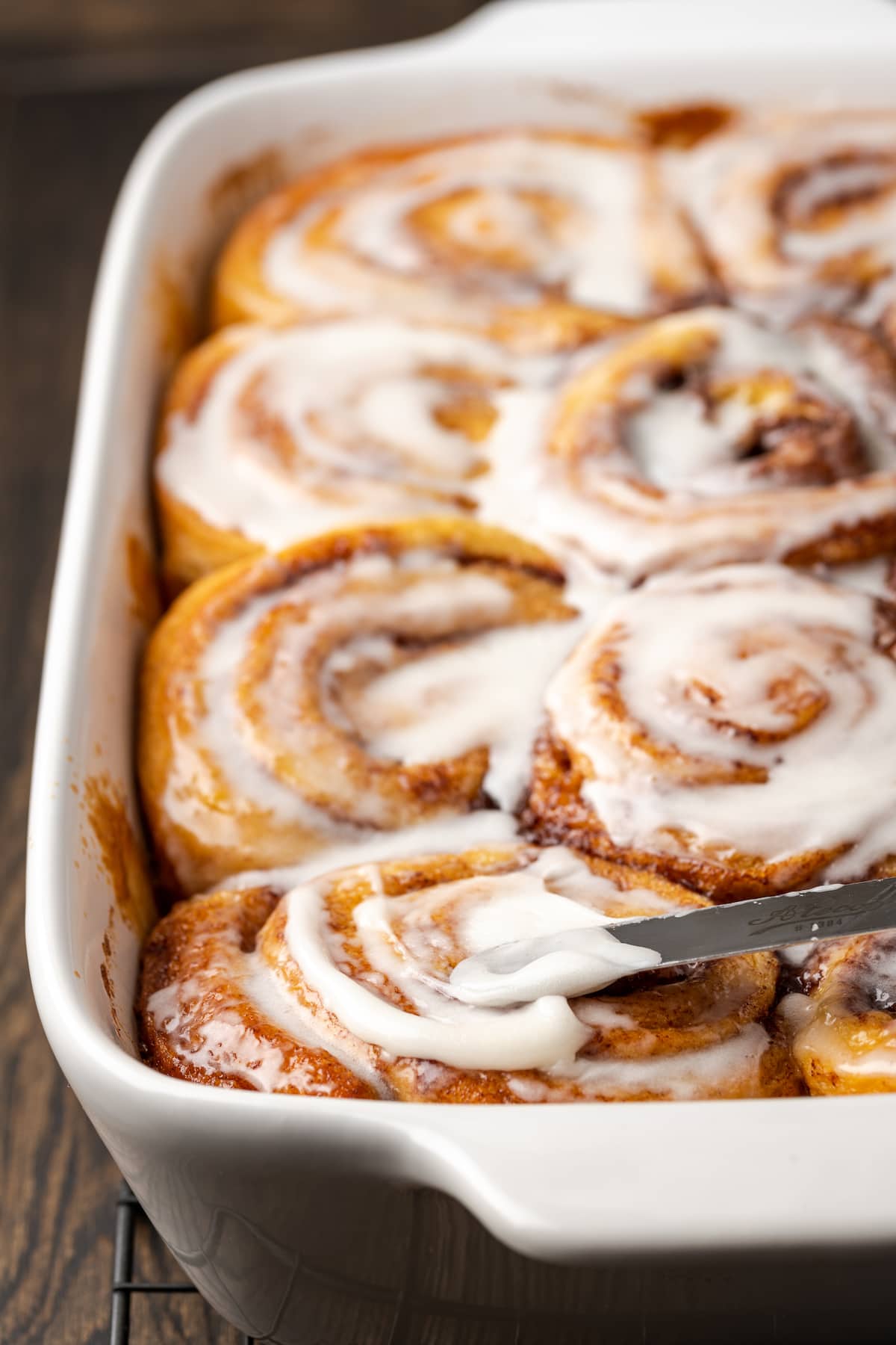 Make the viral TikTok cinnamon rolls with heavy cream! These easy cinnamon rolls taste homemade, perfect as a sweet breakfast or easy dessert. A knife spreading frosting over baked TikTok cinnamon rolls in a ceramic baking dish.