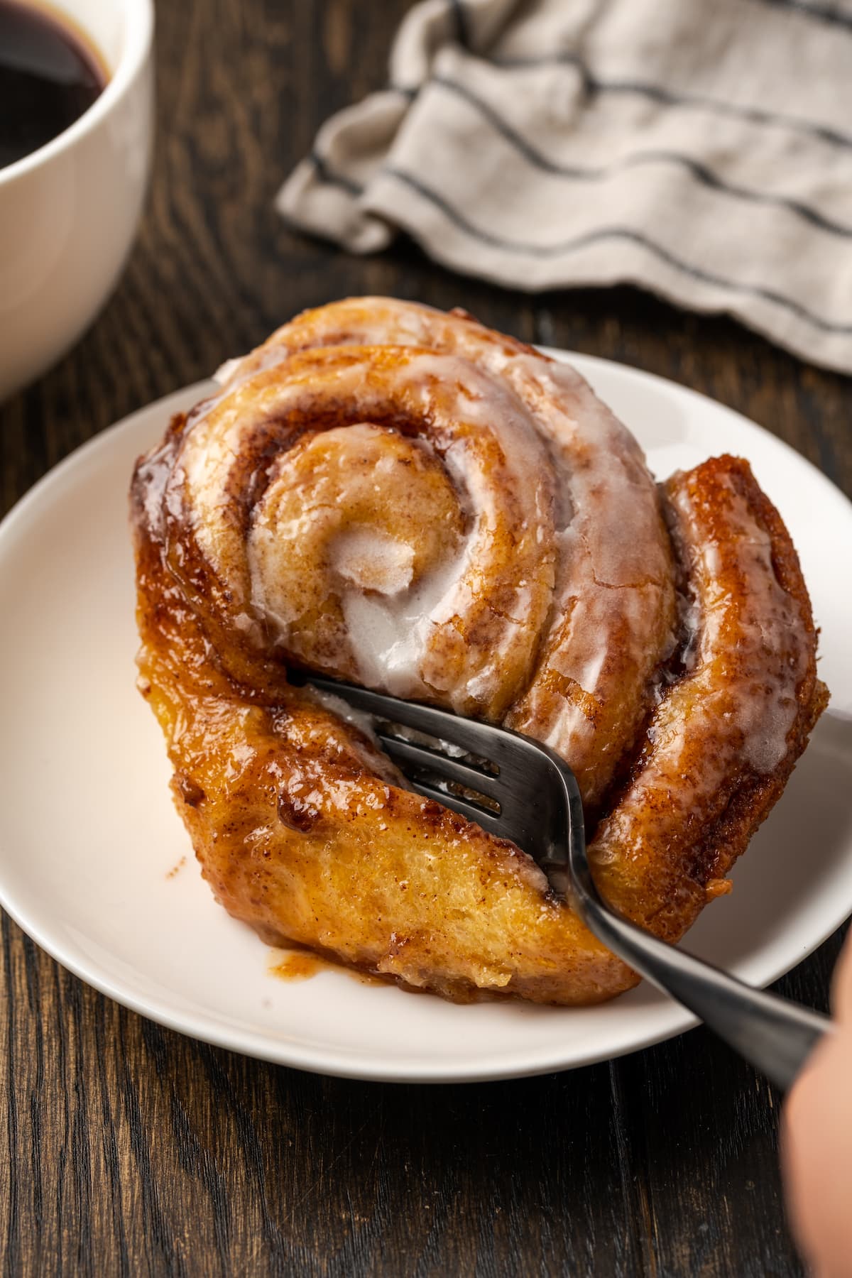 Make the viral TikTok cinnamon rolls with heavy cream! These easy cinnamon rolls taste homemade, perfect as a sweet breakfast or easy dessert. A fork cutting into the corner of a cinnamon roll on a white plate next to a cup of coffee.