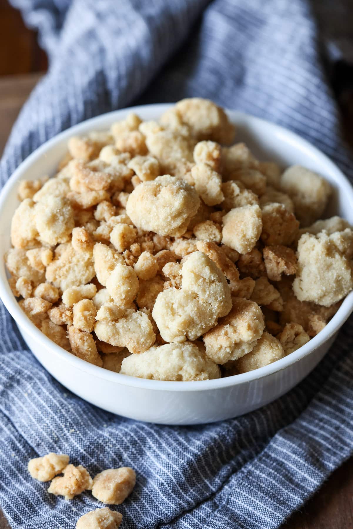 Streusel Topping, también conocido como Crumb Topping, es muy fácil de hacer y se puede usar en muchos productos horneados diferentes, desde muffins y panes hasta pasteles y tartas, ¡o se hornea solo y se usa como una cobertura crujiente de mantequilla! Un tazón blanco lleno de cobertura crujiente de migas horneadas