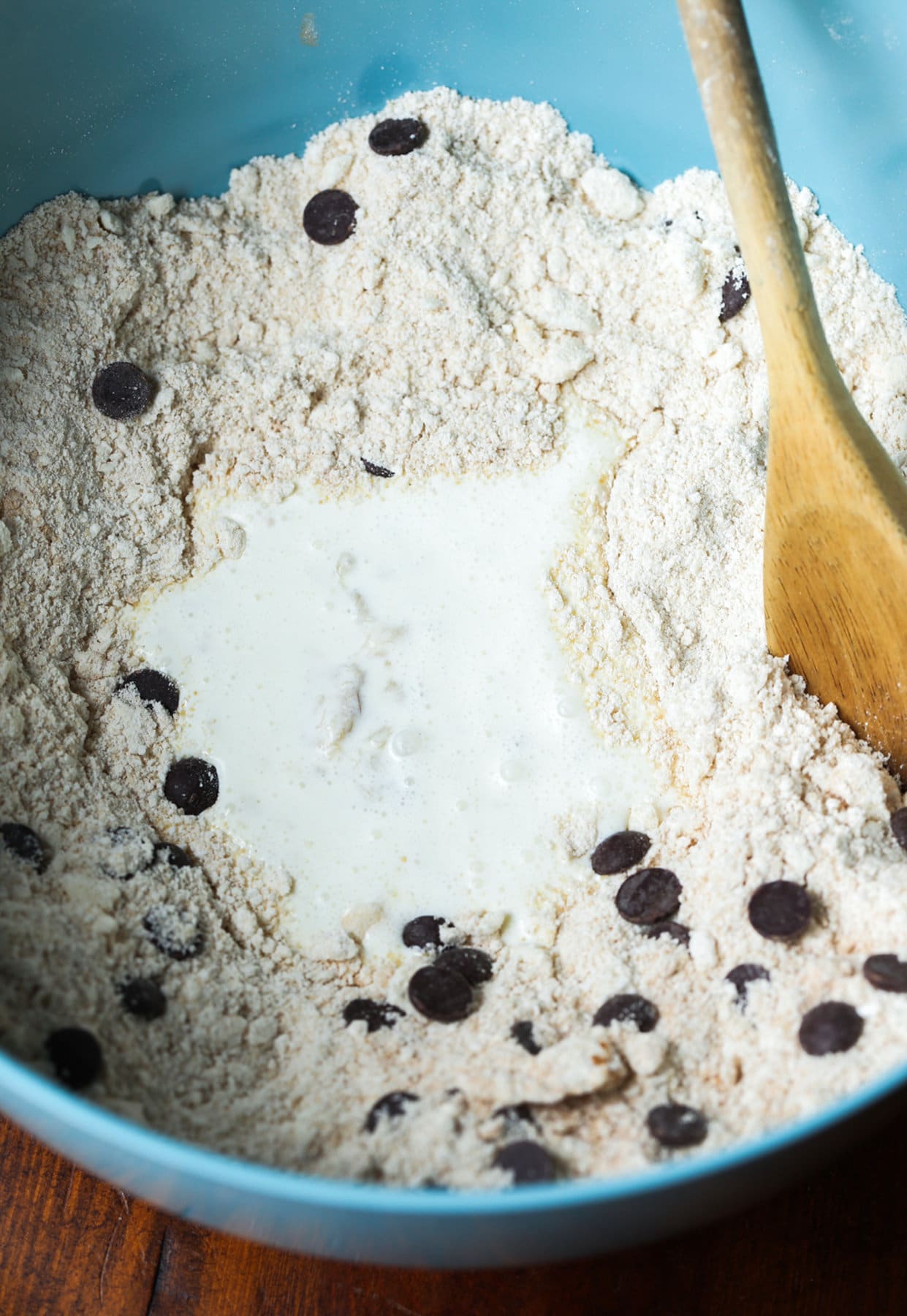 These Chocolate Chip Banana Scones have perfectly crisp, buttery edges with a fluffy, yet flaky, soft center making this the perfect scone recipe! A blue bowl with flour, chocolate chips and heavy cream stirred with a wooden spoon