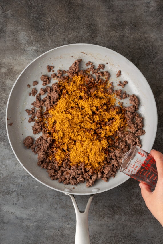 Make satisfying crunch wraps loaded with taco meat, melty cheese, tostada, sour cream, and more wrapped up inside a toasty flour tortilla! Taco seasoning added to a skillet with browned ground beef.