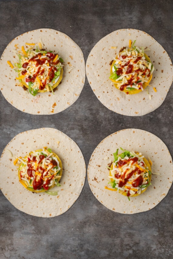 Make satisfying crunch wraps loaded with taco meat, melty cheese, tostada, sour cream, and more wrapped up inside a toasty flour tortilla! Overhead view of four assembled crunch wraps topped with meat, corn tortillas, veggies, and cheese.