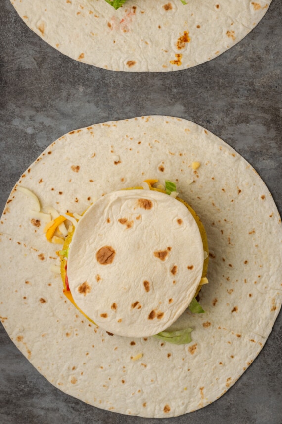 Make satisfying crunch wraps loaded with taco meat, melty cheese, tostada, sour cream, and more wrapped up inside a toasty flour tortilla! A smaller tortilla placed over the fillings of an unfolded crunch wrap.