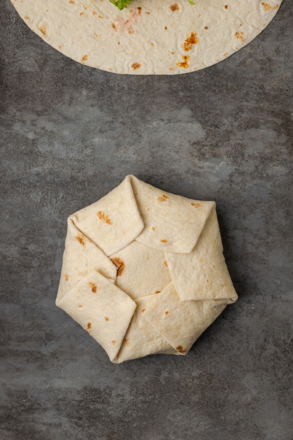 Make satisfying crunch wraps loaded with taco meat, melty cheese, tostada, sour cream, and more wrapped up inside a toasty flour tortilla! A folded crunch wrap on a countertop.