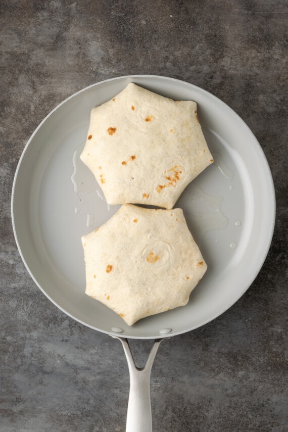 Make satisfying crunch wraps loaded with taco meat, melty cheese, tostada, sour cream, and more wrapped up inside a toasty flour tortilla! Two folded crunch wraps in a skillet.
