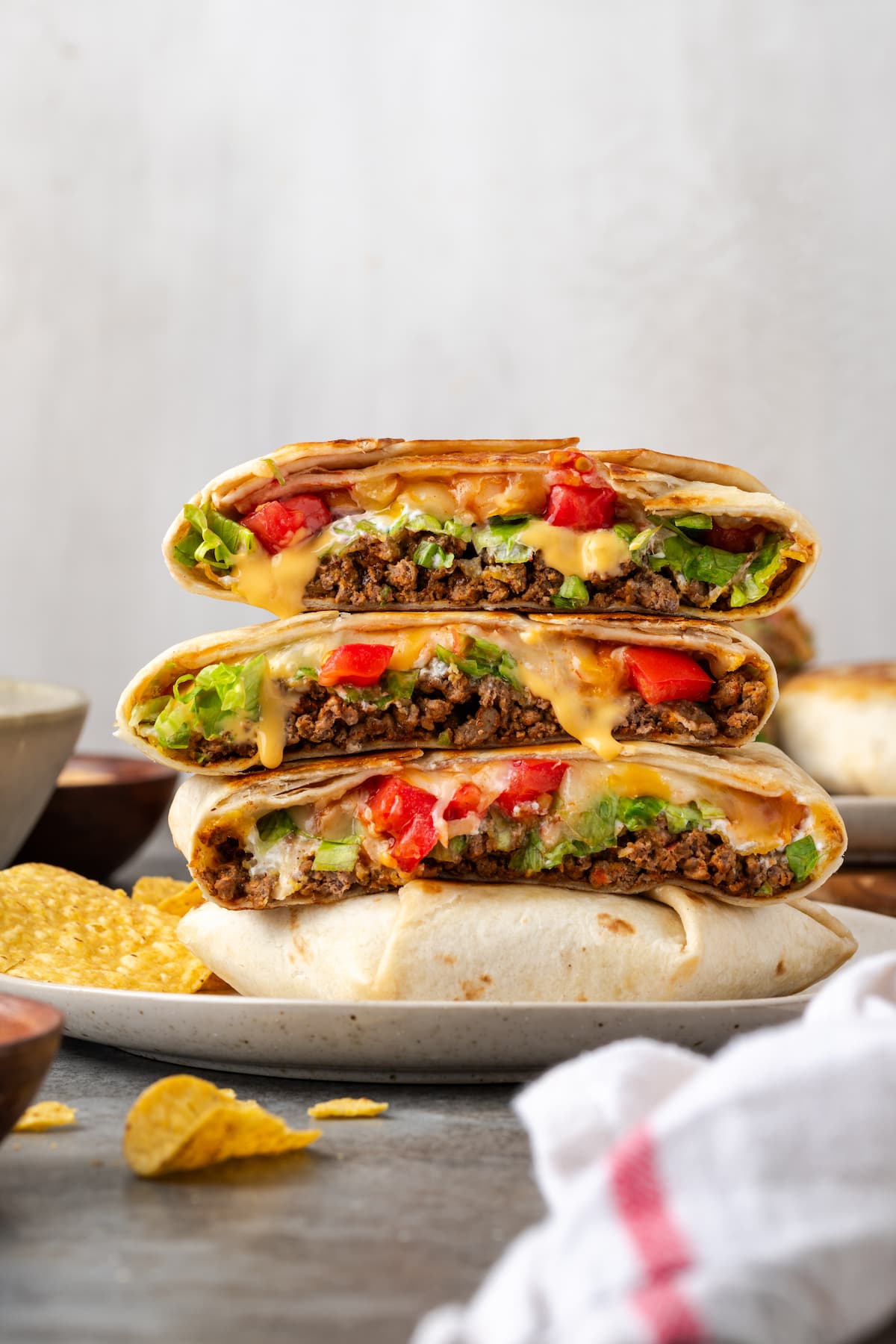 Make satisfying crunch wraps loaded with taco meat, melty cheese, tostada, sour cream, and more wrapped up inside a toasty flour tortilla! Crunch wraps cut in half and stacked on a plate.