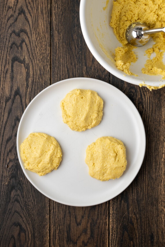 Crispy hot water cornbread is totally crave-worthy! Fried cornbread is an easy side dish to pair with your favorite Southern meals. Three portions of cornbread dough on a plate next to a mixing bowl.