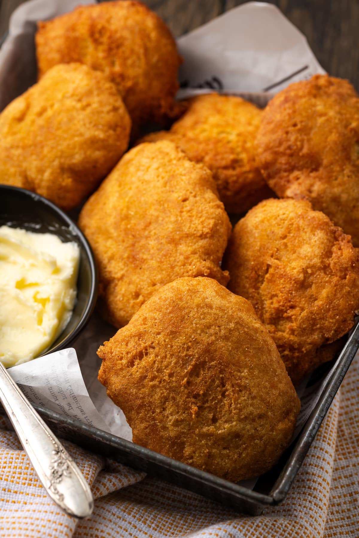 Crispy hot water cornbread is totally crave-worthy! Fried cornbread is an easy side dish to pair with your favorite Southern meals. Close up of hot water cornbread served in a basket next to a small dish of butter, with a knife for spreading.