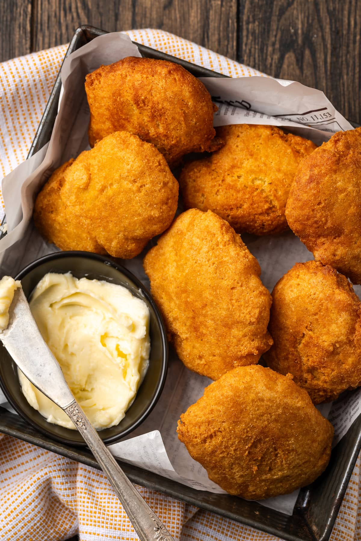 Crispy hot water cornbread is totally crave-worthy! Fried cornbread is an easy side dish to pair with your favorite Southern meals. Overhead view of hot water cornbread served in a basket next to a small dish of butter, with a knife for spreading.